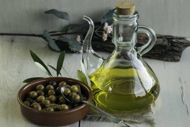 Olive oil and Arbequina olives on birch wood glass bowl to pour olive oil. Also olive tree leaves clipart