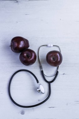 Ahşap arka planda kırmızı elmalarla steteskop