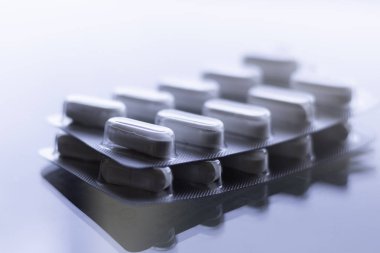 Kapsüllerdeki haplar cam tezgahta ve beyaz arka planda