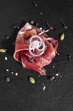 Jamon, baharat ve soğan dilimlenmiş halkalarla siyah bir tabağa yayılır..