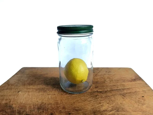 Yellow lemon inside an old glass jar on wooden board. White background — Stock Photo, Image