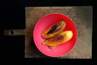 Kırmızı tabakta kızartılmış muz, siyah arka planlı tahta üzerinde. Tipik Guatemala yemekleri.