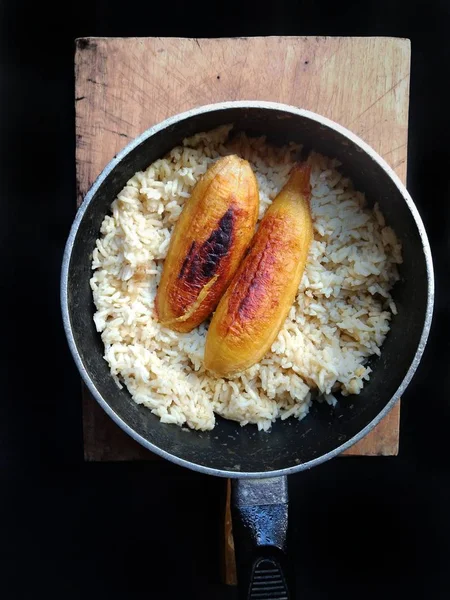 Gefrituurde bananen met rijst op een pot met houten plank met zwarte achtergrond. typische levensmiddelen van Guatemala — Stockfoto