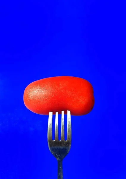 Widelec umieszczony w organicznym pomidorze na niebieskim tle. zdrowa koncepcja żywności — Zdjęcie stockowe