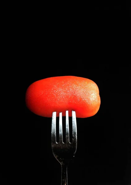 Garfo inserido em um tomate orgânico sobre fundo preto. conceito de alimentação saudável — Fotografia de Stock