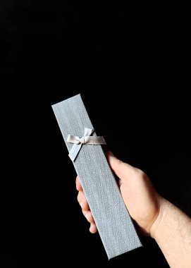 Elinde siyah arka planda bir hediye kutusu var.