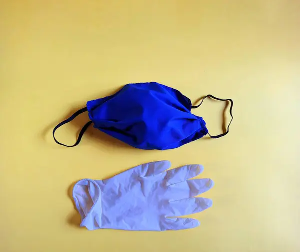 Mavi el yapımı tıbbi maske ve sarı arka planda beyaz lateks eldiven. tıbbi konsept