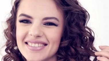 Uzun kıvırcık saçlı, gülümseyen güzel bir kadın. Güzel surat. Moda modeli. Moda makyajı. Göz makyajlı çekici seksi bir kız. Bir kadının yakın çekim yüzü. Yavaş çekim 4k görüntü.   