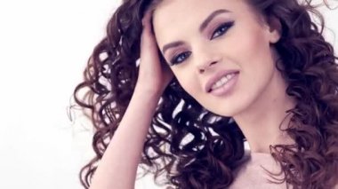 Uzun kıvırcık saçlı, gülümseyen güzel bir kadın. Güzel surat. Moda modeli. Moda makyajı. Göz makyajlı çekici seksi bir kız. Bir kadının yakın çekim yüzü. Yavaş çekim 4k görüntü.   