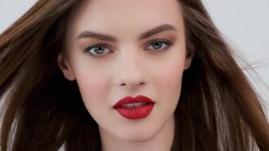 Kırmızı dudaklı güzel bir genç kadının portresi. Uzun düz saçlı, çekici bir kız. Şehvetli manken. Seksi, beyaz bir kızın yakın plan yüzü gibi. 4K görüntü. Yavaş çekim.