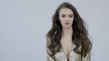 Kıvırcık uzun kahverengi saçlı güzel bir kadının 4K görüntüsü. Moda modeli kameraya bakıyor. Kafkasyalı bir kızın çarpıcı yüzü. Güzel gözleri olan seksi bir manken. Ağır çekim. Güzellik konsepti 