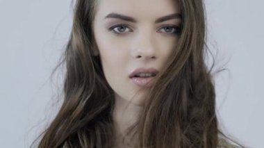 Rüzgarda dalgalanan uzun kahverengi saçlı genç bir kadının 4K görüntüsü. Kız kameraya bakıyor. Kafkasyalı bir kızın çarpıcı yüzü. Kahverengi saçlı, seksi bir manken. Yavaş çekim.