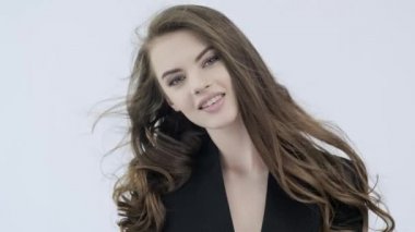 Kıvırcık uzun kahverengi saçlı mutlu genç bir kadının 4K görüntüsü. Neşeli manken kameraya bakıyor. Kafkasyalı bir kızın çarpıcı yüzü. Stüdyoda poz veren neşeli bir model. Yavaş çekim. 