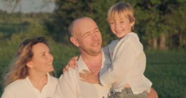 Mutlu çocuklu bir aile yazın çayırda yürüyor. Anne, baba ve 7 yaşındaki oğlu sahada geziniyor. Mutluluk. Yetişkin ebeveynler ve sarışın çocuk doğada başıboş dolaşıyorlar. Yavaş çekim.    