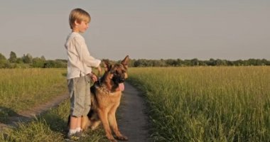 Doğada köpeği olan bir çocuk. 7 yaşında köpek besleyen bir çocuk Alman çoban köpeği besliyor. Sahada köpekle gülümseyen mutlu çocuk. Küçük çocuk çayırda evcil hayvanıyla oynuyor.. 