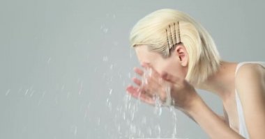 Kadın temiz yüzünü suyla yıkıyor. Genç yetişkin kız yüzünü suyla yıkıyor. Yavaş çekim 4K görüntüsü. Güzellik tedavileri. Cilt bakımı. Sağlıklı cilt kavramı. 