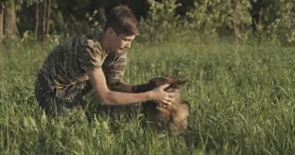 有狗在大自然中的青少年 15岁的男孩爱抚一只德国牧羊犬 和狗一起在球场上快乐地微笑着的少年 白人在草地上和他的宠物玩耍 — 图库视频影像