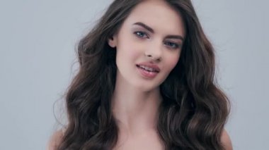 Uzun kıvırcık kahverengi saçlı güzel bir kadın. Moda modeli stüdyodaki kameraya bakıyor. Çekici esmer bir kadının yakın çekim yüzü. Saexy görünüşlü seksi bir manken. 4K görüntü. Yavaş çekim. 