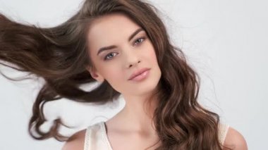 Uzun kıvırcık kahverengi saçlı güzel bir kadın. Moda modeli stüdyodaki kameraya bakıyor. Çekici esmer bir kadının yakın çekim yüzü. Saexy görünüşlü seksi bir manken. 4K görüntü. Yavaş çekim. 