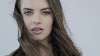 Rüzgarda dalgalanan uzun kahverengi saçlı genç bir kadının 4K görüntüsü. Kız kameraya bakıyor. Kafkasyalı bir kızın çarpıcı yüzü. Kahverengi saçlı, seksi bir manken. Yavaş çekim.