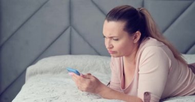 Kötü haberden rahatsız olan yetişkin bir kadın. Güzel yetişkin beyaz kadın akıllı telefonda sohbet ediyor. Kadın kötü bir SMS mesajıyla şoka girdi. Kafkas kadın cep telefonuyla yatakta yatıyor. Gerçek zamanlı.