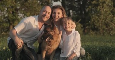 Doğada köpeği olan mutlu bir aile. Ailesiyle birlikte 7 yaşında bir çocuk bir Alman çoban köpeğini besliyor. Sahada köpeklerle gülümseyen bir aile. İnsanlar evcil hayvanıyla çayırdalar. Yavaş çekim