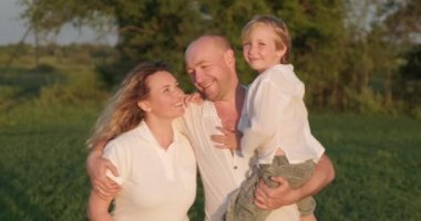 Mutlu çocuklu bir aile yazın çayırda yürüyor. Anne, baba ve 7 yaşındaki oğlu sahada geziniyor. Mutluluk. Yetişkin ebeveynler ve sarışın çocuk doğada başıboş dolaşıyorlar. Yavaş çekim.    