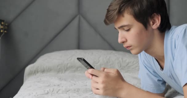 十代の若者はその悪い知らせに腹を立てた 十代の少年は悪いSmsメッセージにショックを受けています 白人の青年はうつ状態になり顔を隠す 白人の学生は携帯電話でベッドの上に横たわっていた リアルタイム — ストック動画
