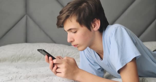 十代の若者はその悪い知らせに腹を立てた 十代の少年は悪いSmsメッセージにショックを受けています 白人の青年はうつ状態になり顔を隠す 白人の学生は携帯電話でベッドの上に横たわっていた リアルタイム — ストック動画