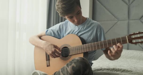 年轻的男人在家里弹吉他 一个拿着木吉他的少年坐在沙发上 孩子们弹吉他 年轻人用一把古典吉他弹奏 实时录像 — 图库视频影像