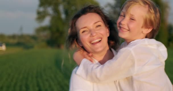 快乐的母亲牵着她的儿子在草地上散步 母亲和7岁的儿子在田里散步 有孩子的成年母亲在大自然中漫游和欢笑 慢动作 — 图库视频影像