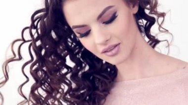 Uzun kıvırcık saçlı güzel bir kadın. Güzel surat. Moda modeli. Moda makyajı. Göz makyajlı çekici bir kız. Bir kızın yakın çekim yüzü. Yavaş çekim 4K görüntüsü. Seksi esmer bayan..  