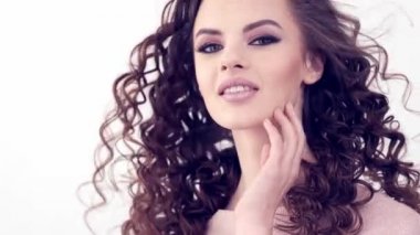 Uzun kıvırcık saçlı, gülümseyen güzel bir kadın. Güzel surat. Moda modeli. Moda makyajı. Göz makyajlı çekici seksi bir kız. Bir kadının yakın çekim yüzü. Yavaş çekim 4k görüntü.   