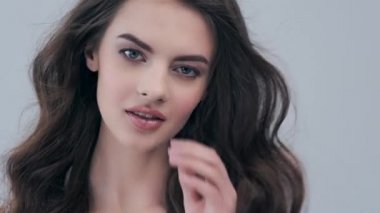 Uzun kıvırcık kahverengi saçlı güzel bir kadın. Moda modeli stüdyodaki kameraya bakıyor. Çekici esmer bir kadının yakın çekim yüzü. Saexy görünüşlü seksi bir manken. 4K görüntü. Yavaş çekim. 