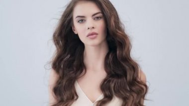 Uzun kıvırcık kahverengi saçlı güzel bir kadın. Moda modeli stüdyodaki kameraya bakıyor. Çekici esmer bir kadının yakın çekim yüzü. Saexy görünüşlü seksi bir manken. 4K görüntü. Yavaş çekim. 