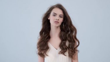Uzun kıvırcık kahverengi saçlı güzel bir kadın. Moda modeli stüdyodaki kameraya bakıyor. Çekici esmer bir kadının yakın çekim yüzü. Saexy görünüşlü seksi bir manken. 4K görüntü. Yavaş çekim. 