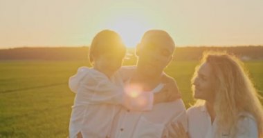 Mutlu aile yazın çayırda yürüyor. Anne, baba ve 7 yaşındaki oğlu sahada geziniyor. Mutluluk kavramı. Yetişkin ebeveynler ve sarışın çocuk doğada başıboş dolaşıyorlar. Yavaş çekim.    