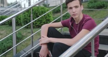Ergen kulaklıkla müzik dinliyor. Kendine güvenen genç yakışıklı adam açık havada, kulaklıkla müzik dinliyor. Kulaklıklı güzel bir gencin portresi. Şehir manzarası. 4 bin. Gerçek zamanlı..  