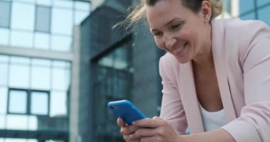 Yetişkin bir kadın cep telefonundan mesaj yazıyor. Gülümseyen iş kadını dışarıda cep telefonuyla mesaj atıyor. Cep telefonlu mutlu bir bayan. Gerçek zamanlı. 4k.         
