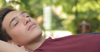 Parktaki bankta uzanmış, kulaklıklı genç bir çocuğun portresi. Ergen kulaklıkla müzik dinliyor. Genç yakışıklı adam kulaklıkla açık havada müzik dinliyor.. 