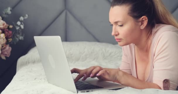 在家里的笔记本电脑上工作的成年妇女 一个带着电脑在沙发上的成年女人 白人妇女在笔记本电脑上输入消息 生活方式的概念 严肃的女人看着手提电脑上的监视器 — 图库视频影像