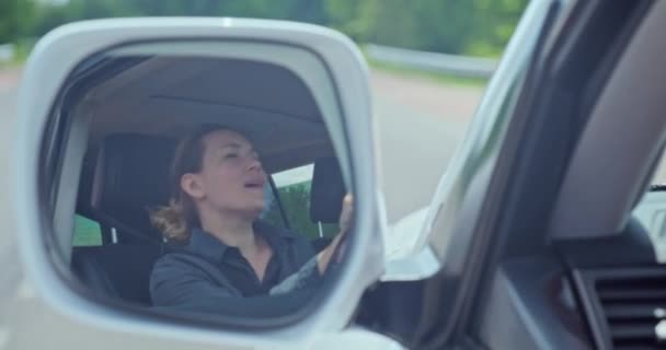 女は車を運転して歌を歌う 美しい大人の陽気な女性が車を運転しています 白人の少女は自動車を運転しながら音楽を聴く 女性の運転車の外車のミラーの反射 — ストック動画