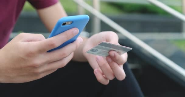 人々は屋外のクレジットカードおよび携帯電話を使用してオンライン購入をする 人間の手は銀行カードで携帯電話を持っています 男性の手はオンラインショッピングにスマートフォンやクレジットカードを使用します — ストック動画
