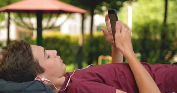 Portrait Happy Teenage Boy Talking Mobile Phone Lying Bench Park — Stock Video