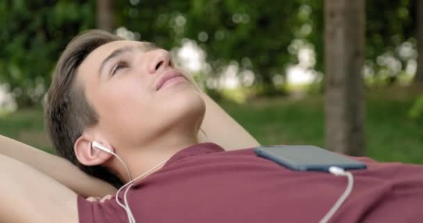 Портрет Счастливого Подростка Наушниках Лежащего Скамейке Парке Расслабляющего Подросток Слушает — стоковое видео