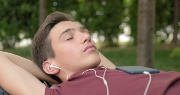 Портрет Подростка Наушниках Лежащего Скамейке Парке Расслабляющего Подросток Слушает Музыку — стоковое видео
