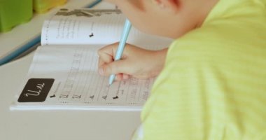 Mektupları okul defterine yazan çocuk. Öğrenci evde el yazısıyla ödev yapıyor. Mektupları okul çocuğu yazıyor. Çocuk okuldan sonra ev ödevi yapar. Gerçek zamanlı. 4k görüntü     