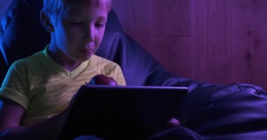 Gülümseyen çocuk tablete bakar ve elma yer. Akşamları tabletli şirin bir çocuk. Kafkasyalı mutlu çocuk tablet tutuyor. Öğrenci internet 'te vakit geçiriyor. Gerçek zamanlı. Yakınlaştır 