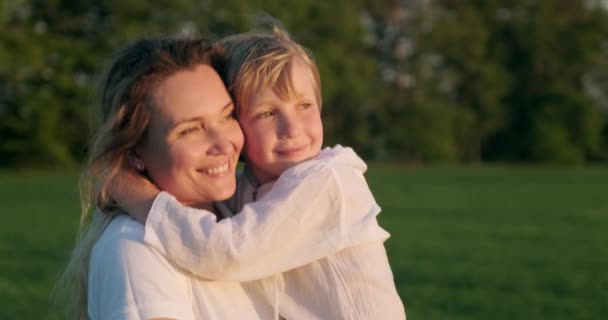 幸せな母親は夏に牧草地を歩いて彼女の息子を手に持っています 7歳の子供を持つ母親はフィールドに散歩します 金髪の男の子と大人の母親が自然の中でサンザリング スローモーション — ストック動画
