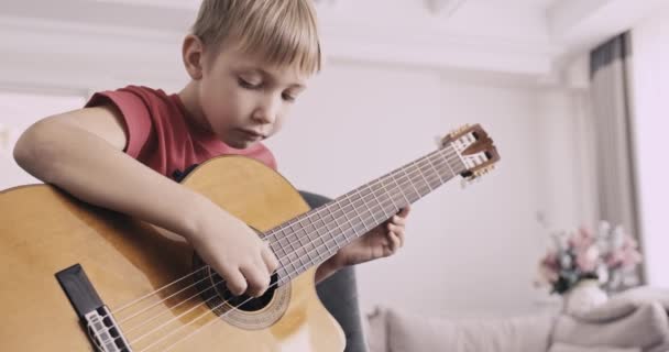 一个拿着吉他的小男孩 8岁的男孩弹古典吉他 这个高加索小孩学会了弹吉他 放大放大 自然光 低角度视图 — 图库视频影像